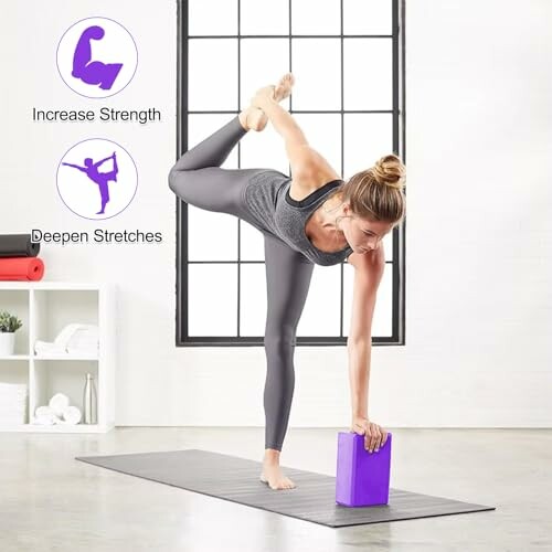 Mujer haciendo yoga con bloque morado en una sala luminosa.